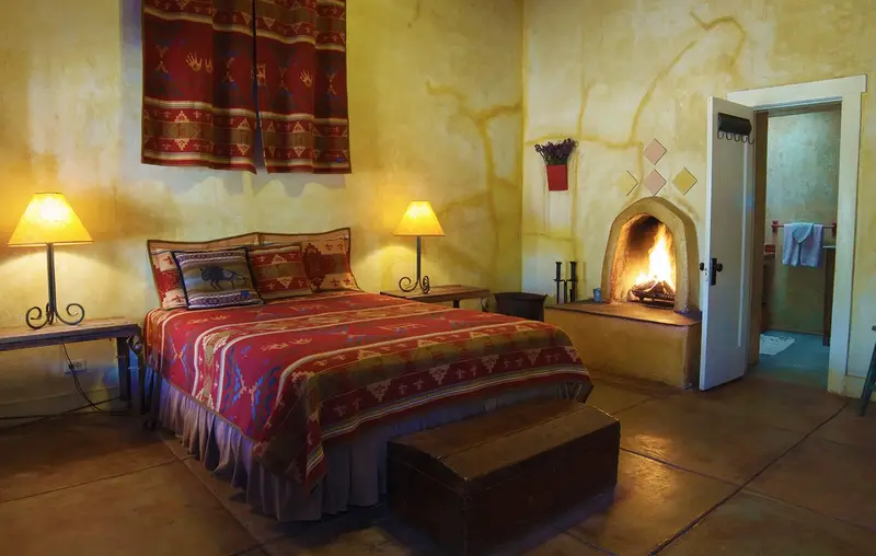 A queen room with a Navajo rug above the bed and a kiva fireplace