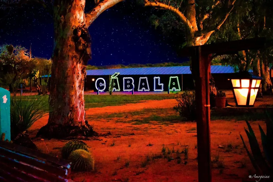 The neon Cábala sign glowing on an adobe wall under a desert night sky